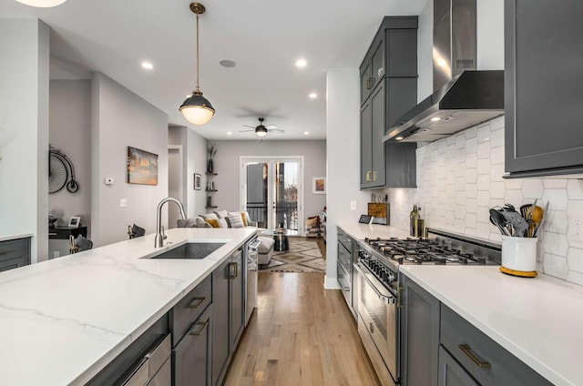 kitchen featuring light wood finished floors, stainless steel appliances, decorative backsplash, a sink, and wall chimney range hood