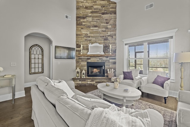 living room with a high ceiling, a stone fireplace, and dark wood-type flooring