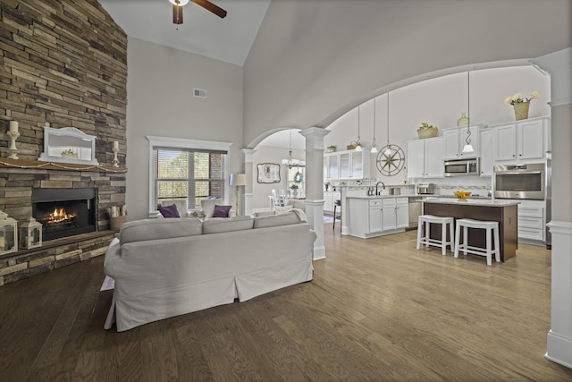 living room featuring sink, ornate columns, ceiling fan, a fireplace, and hardwood / wood-style floors