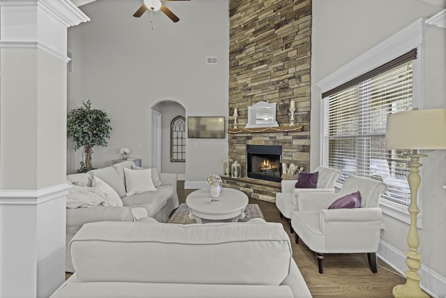 living room featuring a high ceiling, a stone fireplace, hardwood / wood-style floors, and ceiling fan