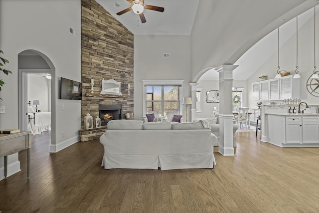 living room featuring ornate columns, wood-type flooring, a fireplace, and ceiling fan