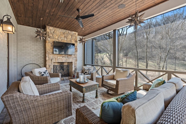 sunroom featuring ceiling fan, an outdoor stone fireplace, and wooden ceiling