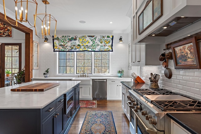 kitchen featuring wall chimney range hood, appliances with stainless steel finishes, hanging light fixtures, a wealth of natural light, and white cabinets