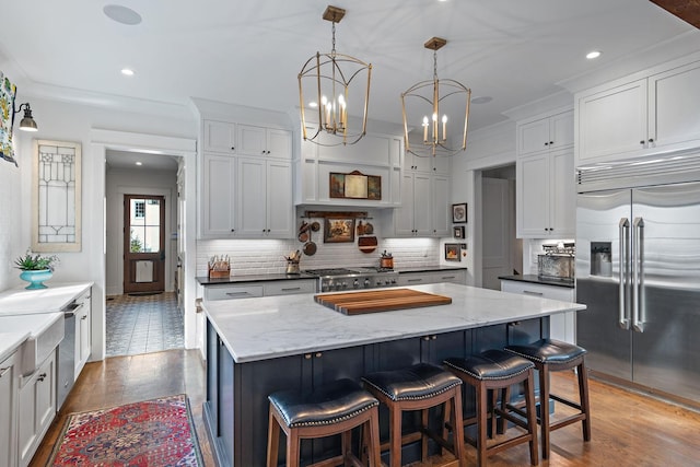 kitchen with white cabinetry, built in refrigerator, a center island, ornamental molding, and pendant lighting