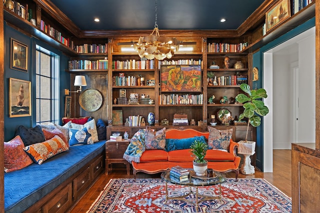 living area with ornamental molding, hardwood / wood-style floors, and a notable chandelier