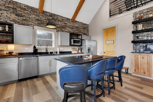 kitchen featuring pendant lighting, sink, beam ceiling, stainless steel appliances, and light hardwood / wood-style floors