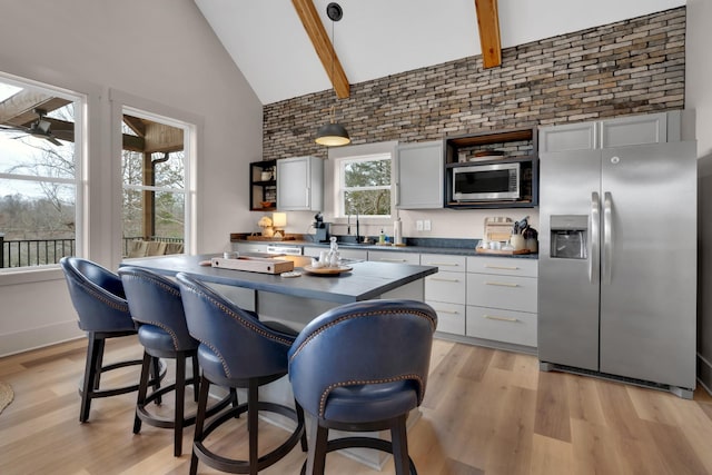 kitchen featuring stainless steel appliances, white cabinets, beam ceiling, and light hardwood / wood-style floors