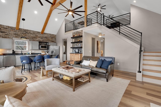 living room featuring sink, high vaulted ceiling, light hardwood / wood-style flooring, beamed ceiling, and ceiling fan