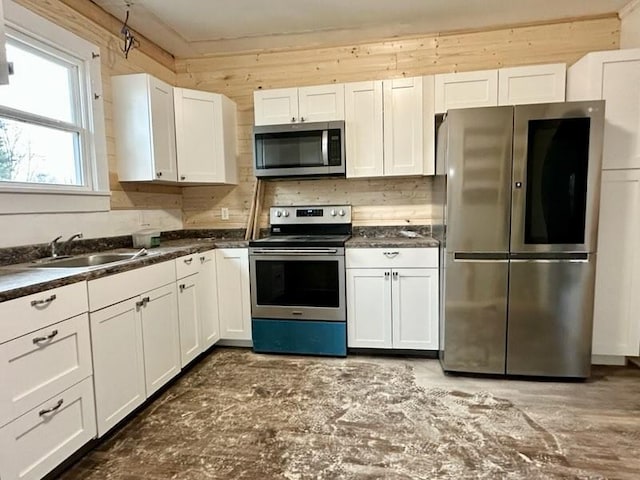 kitchen featuring wood walls, stainless steel appliances, sink, and white cabinets