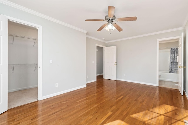 unfurnished bedroom with a walk in closet, ornamental molding, a closet, hardwood / wood-style flooring, and ceiling fan