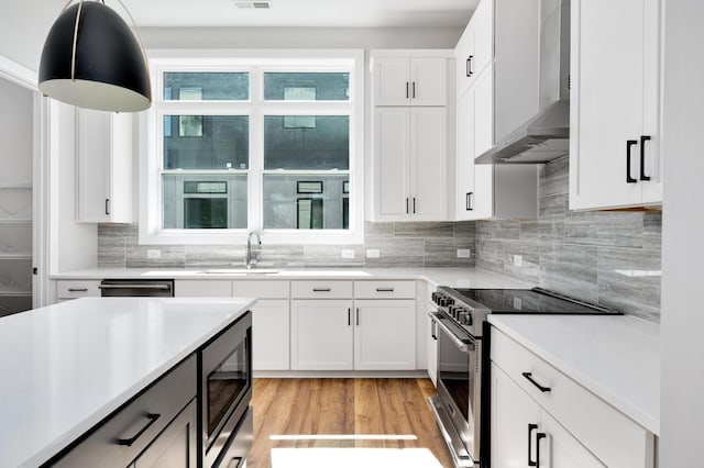 kitchen with wall chimney range hood, sink, appliances with stainless steel finishes, white cabinetry, and decorative light fixtures