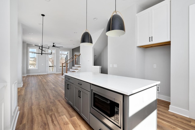 kitchen with white cabinetry, light wood-type flooring, stainless steel microwave, gray cabinets, and pendant lighting