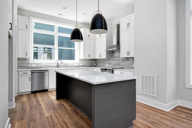 kitchen featuring dark wood-type flooring, wall chimney exhaust hood, white cabinetry, a center island, and stainless steel appliances