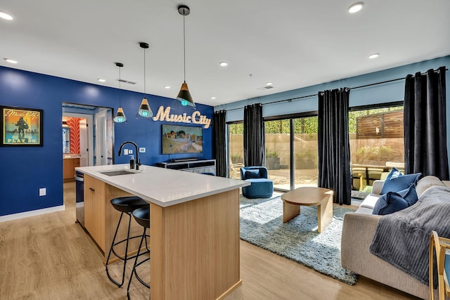 kitchen with sink, decorative light fixtures, an island with sink, and light wood-type flooring