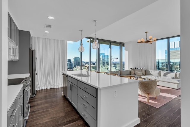 kitchen with appliances with stainless steel finishes, sink, a wall of windows, hanging light fixtures, and a kitchen island with sink