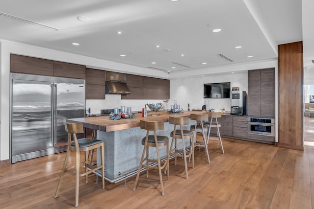 kitchen with appliances with stainless steel finishes, a kitchen bar, butcher block countertops, and light hardwood / wood-style flooring