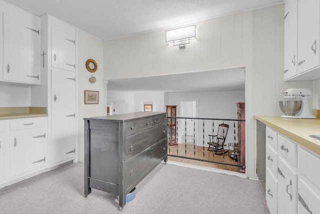 kitchen with light colored carpet, white cabinets, and a textured ceiling