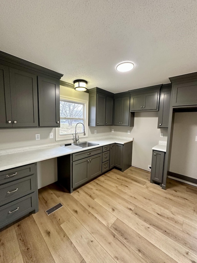 kitchen featuring gray cabinets, sink, a textured ceiling, and light hardwood / wood-style flooring