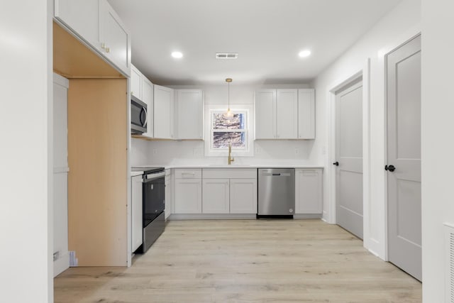 kitchen featuring appliances with stainless steel finishes, sink, white cabinets, hanging light fixtures, and light hardwood / wood-style flooring