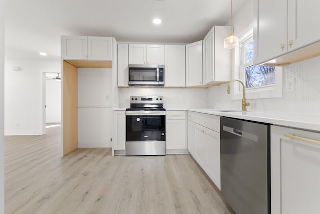 kitchen with white cabinetry, stainless steel appliances, sink, and hanging light fixtures