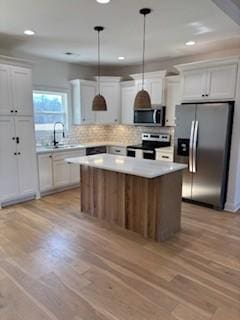 kitchen featuring pendant lighting, appliances with stainless steel finishes, white cabinetry, light hardwood / wood-style floors, and a kitchen island