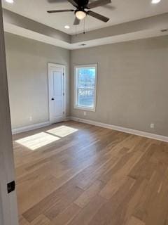 spare room with a raised ceiling, wood-type flooring, and ceiling fan