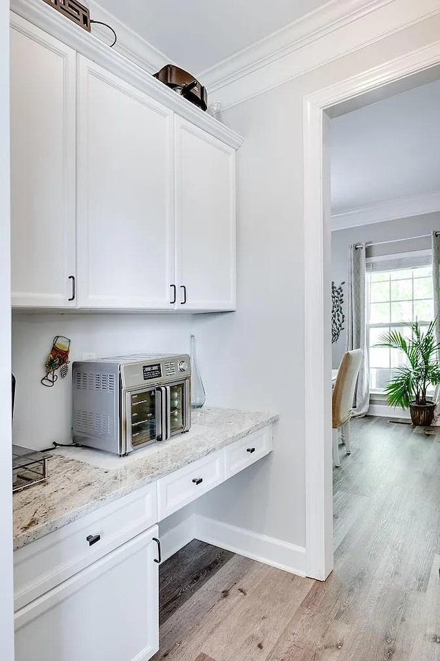 bar featuring light stone counters, ornamental molding, light hardwood / wood-style flooring, and white cabinets