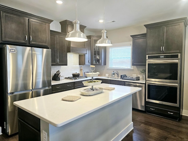 kitchen featuring dark wood-type flooring, tasteful backsplash, hanging light fixtures, a kitchen island, and stainless steel appliances