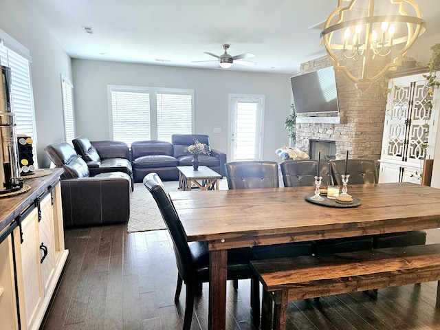 dining space featuring dark hardwood / wood-style flooring, ceiling fan with notable chandelier, and a fireplace