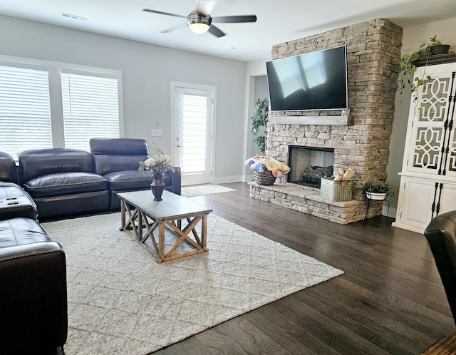 living room featuring ceiling fan, a stone fireplace, and dark hardwood / wood-style flooring