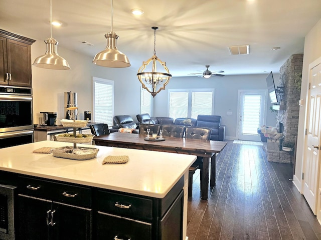 kitchen with decorative light fixtures, a center island, ceiling fan, dark wood-type flooring, and stainless steel double oven