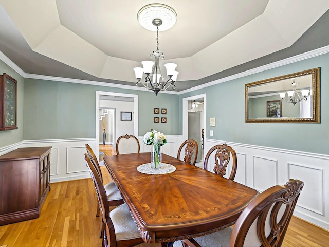 dining space with a chandelier, a raised ceiling, and light hardwood / wood-style flooring