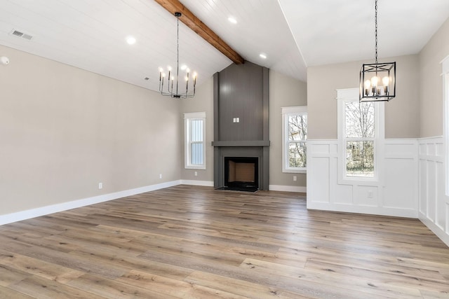 unfurnished living room featuring a large fireplace, a chandelier, lofted ceiling with beams, and light hardwood / wood-style flooring