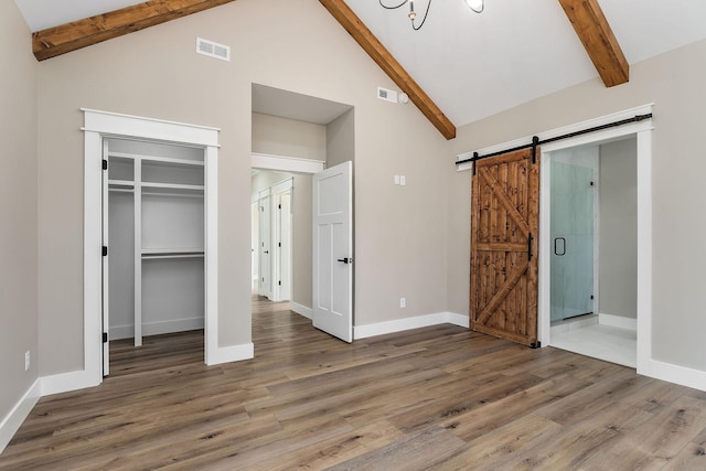 unfurnished bedroom featuring high vaulted ceiling, hardwood / wood-style flooring, a barn door, beam ceiling, and a closet