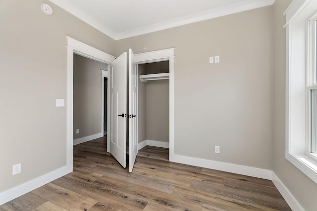 unfurnished bedroom featuring hardwood / wood-style flooring, ornamental molding, and a closet