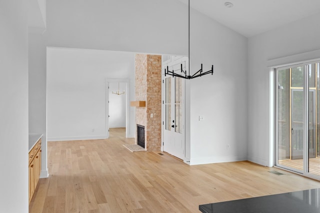 unfurnished living room with a large fireplace, a notable chandelier, and light wood-type flooring