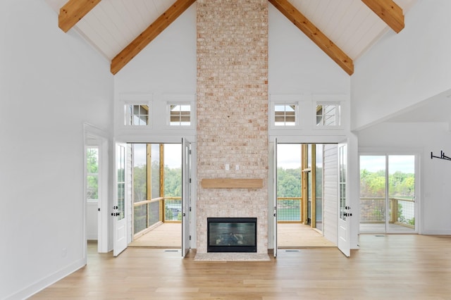 unfurnished living room featuring a stone fireplace, high vaulted ceiling, beam ceiling, and light hardwood / wood-style floors