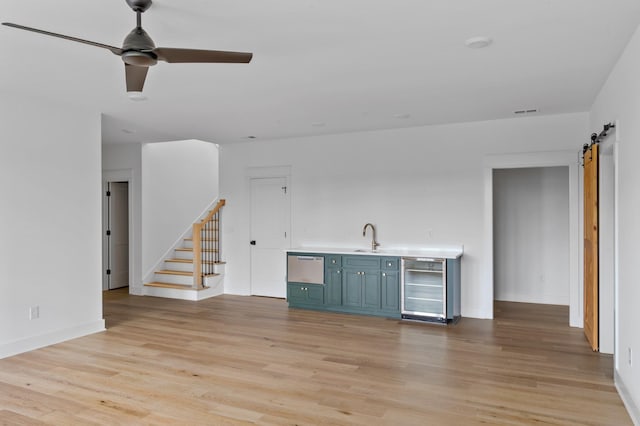 bar with a barn door, wine cooler, ceiling fan, and light hardwood / wood-style flooring