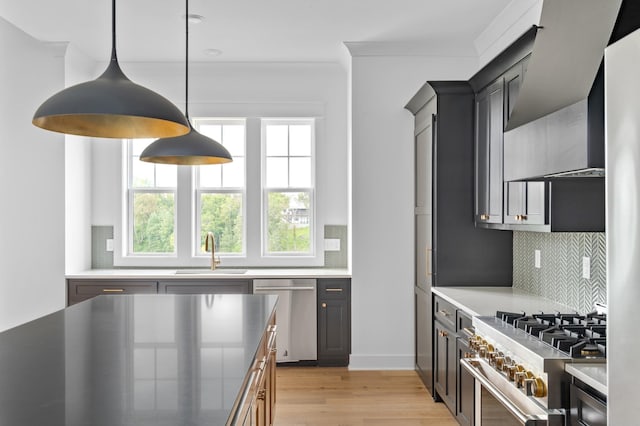 kitchen featuring appliances with stainless steel finishes, pendant lighting, sink, wall chimney range hood, and light hardwood / wood-style flooring