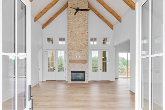 unfurnished living room featuring a fireplace, light hardwood / wood-style floors, french doors, and beamed ceiling