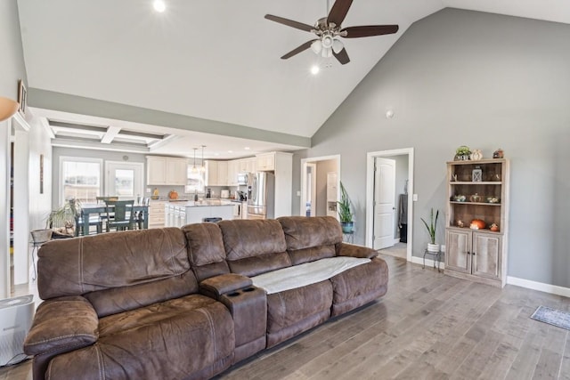 living room with ceiling fan, coffered ceiling, high vaulted ceiling, and light wood-type flooring