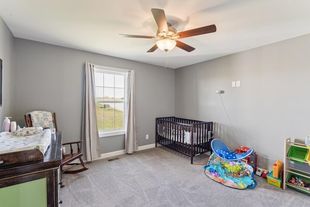 carpeted bedroom featuring a nursery area and ceiling fan