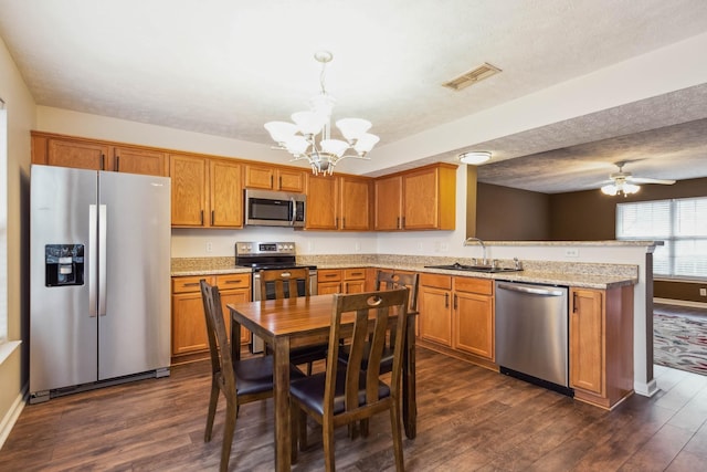 kitchen featuring sink, dark wood-type flooring, hanging light fixtures, stainless steel appliances, and a textured ceiling