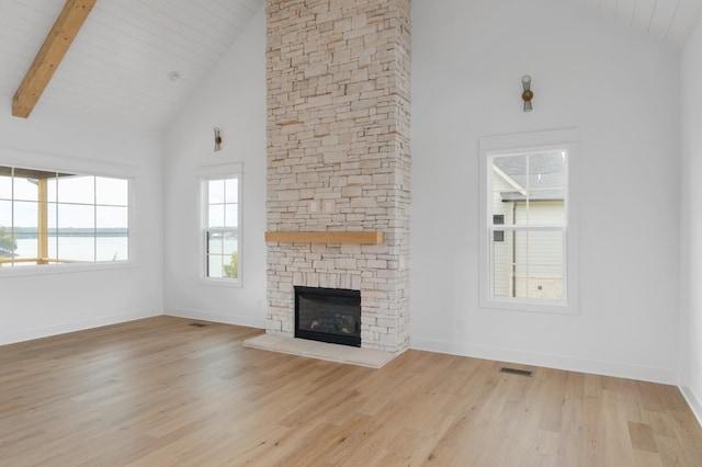 unfurnished living room with beam ceiling, a stone fireplace, high vaulted ceiling, and light hardwood / wood-style flooring