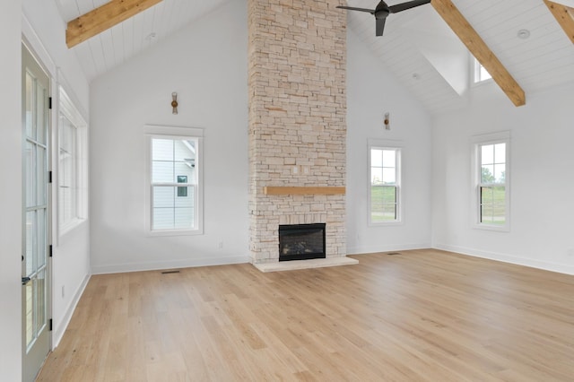 unfurnished living room with a stone fireplace, high vaulted ceiling, ceiling fan, light hardwood / wood-style floors, and beam ceiling