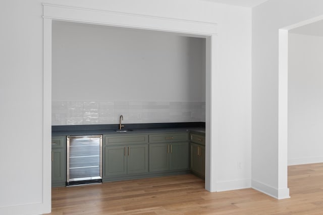 bar with green cabinetry, beverage cooler, light hardwood / wood-style floors, and sink