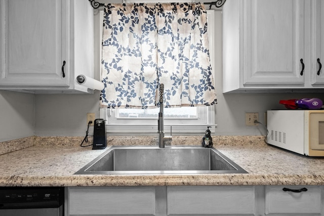 kitchen featuring sink, stainless steel dishwasher, white cabinets, and light stone counters