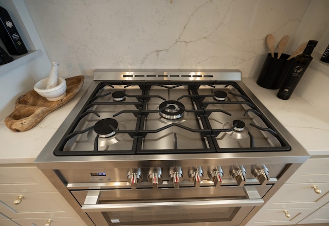 details featuring stainless steel gas stove, decorative backsplash, light stone countertops, and white cabinets