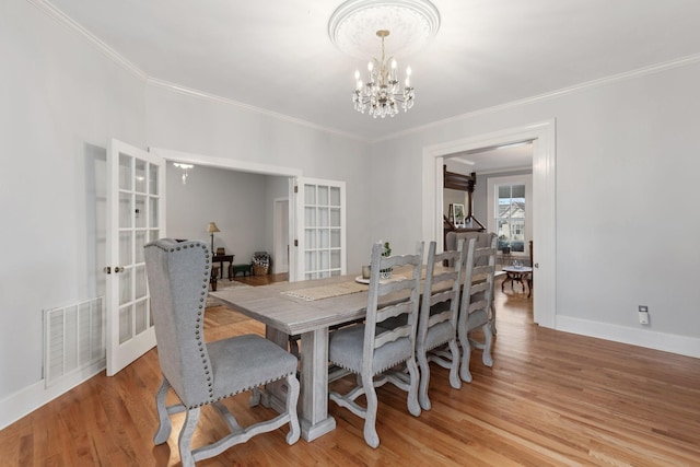 dining space featuring an inviting chandelier, ornamental molding, light hardwood / wood-style floors, and french doors