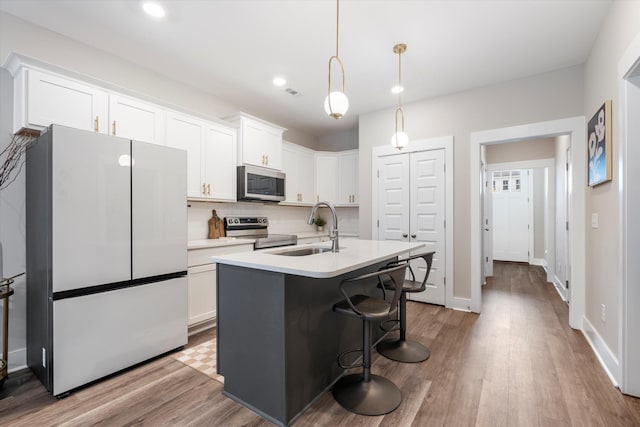 kitchen featuring pendant lighting, white cabinetry, an island with sink, sink, and stainless steel appliances